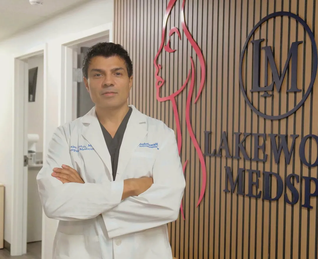 Dr. Rajan Kohli, MD, in a white coat in front of the Lakewood Med Spa wall in Dallas